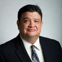 Latino man, short dark hair, wearing white shirt, striped tie, and black jacket smiling at the camera